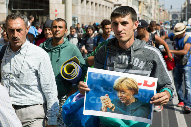 Bei einer Demonstration trägt ein Mann ein Plakat, welches Angela Merkel zeigt