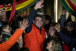 Ein Mann mit einer orangefarbenene Weste winkt, umringt von Anhängern