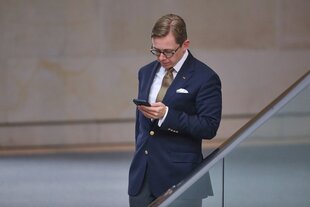 Philipp Amthor steht in einem Flur im Deutschen Bundestag und blickt auf sein Handy