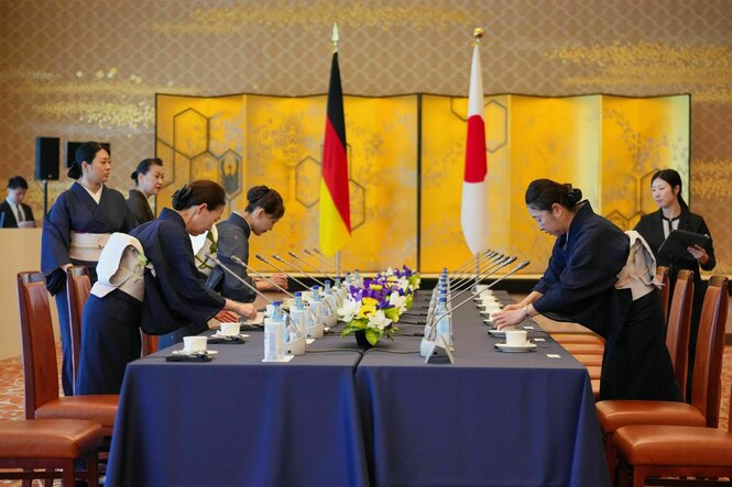 In Tokios Außenministerium bereiten Mitarbeiterinnen im Kimono den Tisch für das Treffen mit dem deutschen Außenminister Wadephul vor. Im Hintergrund die deutsche und japanische Flagge.