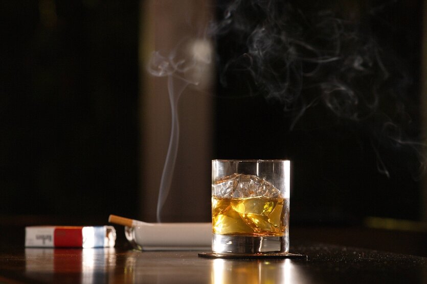 Zigarettenpackung, eine brennende Zigarette und ein Whiskeyglas auf einem Tresen