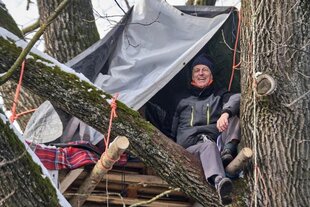Professor Wolfgang Ertel sitzt auf einer mit Seilen im Baum befestigten Plattform unter einem Zeltdach und lächelt in die Kamera.