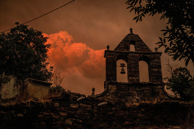 Ein Glockenturm vor dramatischen Wolkenhimmel in rotem Feuerschein