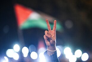 Eine Hand formt ein Peace-Zeichen vor eine Palästina-Fahne