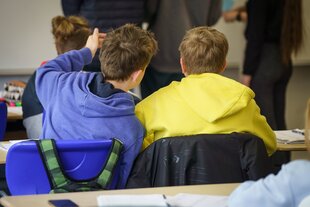 Zwei SChüler im Unterricht: einer trägt ein blaue, der andere eine gelbe Jacke