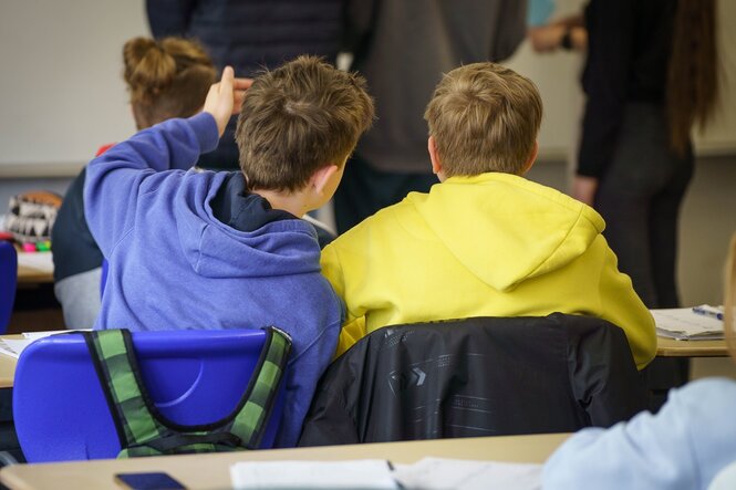 Zwei SChüler im Unterricht: einer trägt ein blaue, der andere eine gelbe Jacke