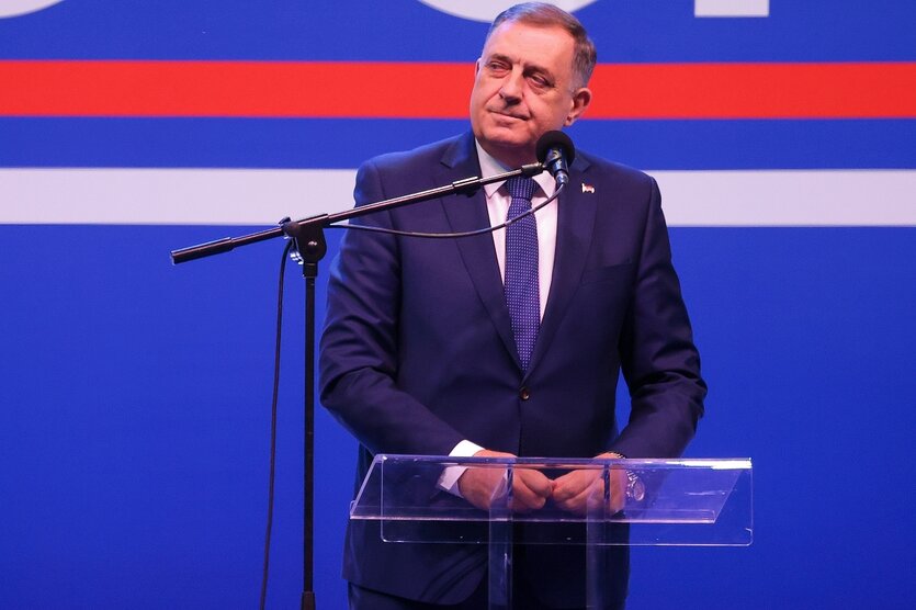 Mann mit Anzug und Krawatte hinter einem gläsernen Rednerpult