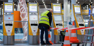 Mann in Warnweste spannt Baustellenband vor Ticket-Automaten
