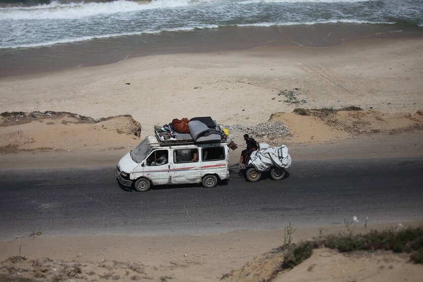 Ein mit Hausrat beladener Kleinbus mit Anhänger fährt am Strand entlang