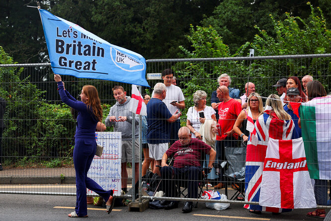 Menschen protestieren, eine Demonstrantin trägt eine Fahne, man kann die Worte "Britain" und "Great" darauf lesen