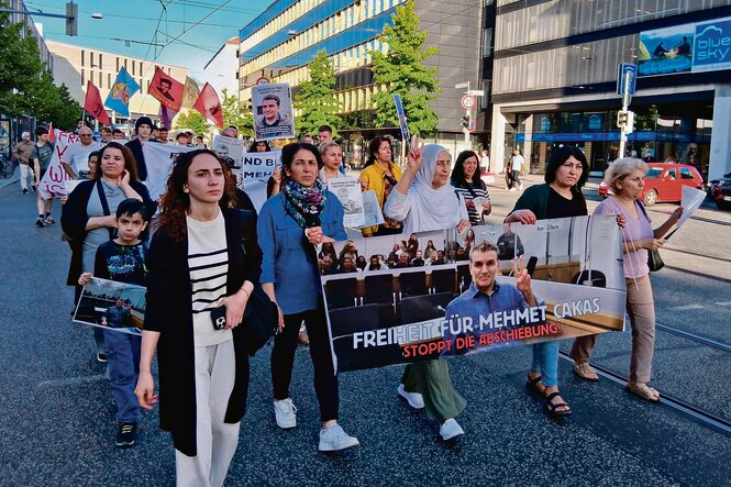 Menschen auf einer Demonstration gegen die Abschiebung von Mehmet Çakas halten ein Transparent und Fahnen