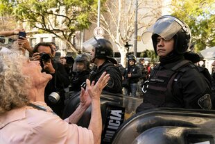 Eine Rentnerin fleht einen behelmten Polizisten in der Nähe des Kongressgebäudes an.
