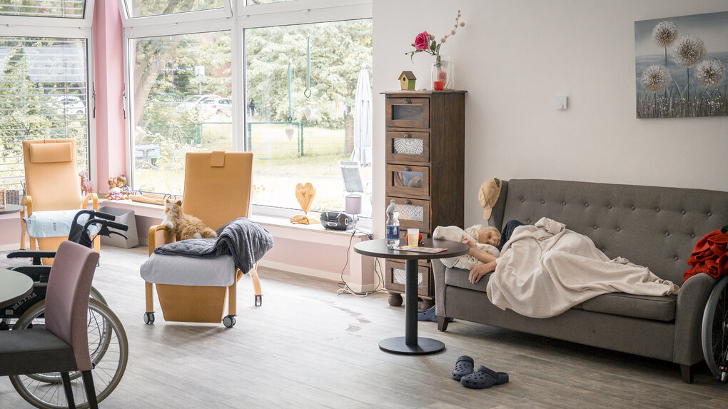 Das Wohnzimmer der Gammeloase: Auf einem Sofa schläft eine Bewohnerin.