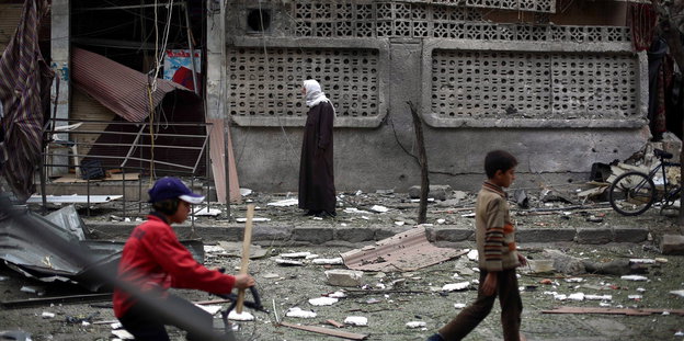 Eine Frau und zwei Kinder laufen durch eine zerstörte Straße.