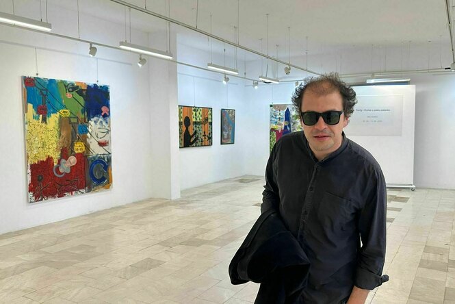 Maler Mili Đukić mit Sonnenbrille in einer hellen Galerie mit Bildern