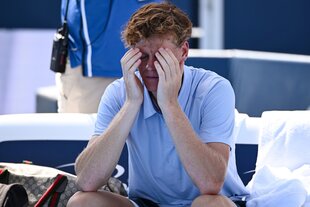 Ein junger Mann im Tennis-Outfit sitzt im Court total erschöpft auf seiner Bank