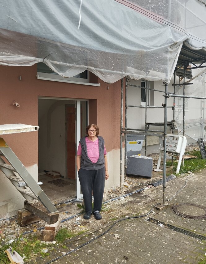 Eine Frau steht vor einem Haus, inmitten einer Baustelle