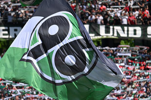 Menschen auf einer Tribüne schwenken grün-weiße Fahnen
