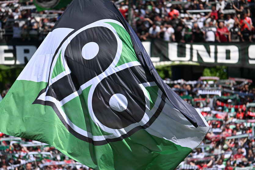 Menschen auf einer Tribüne schwenken grün-weiße Fahnen