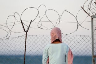 Eine Frau steht vor einem Stacheldrahtzaun