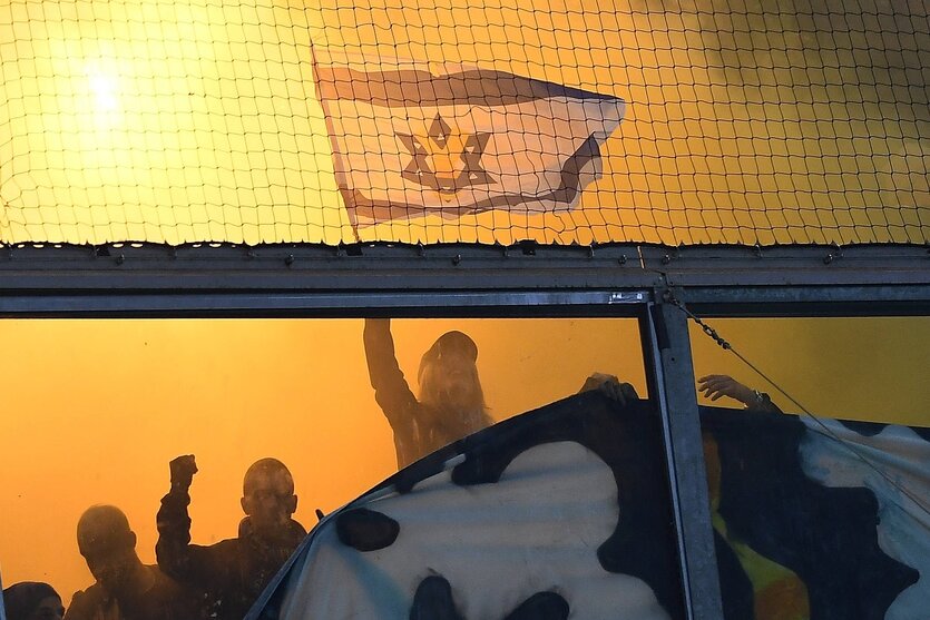 Eine Fankurve im Stadion, im Hintergrund brennt es und im Vordergrund hält jemand eine Israel-Flagge hoch