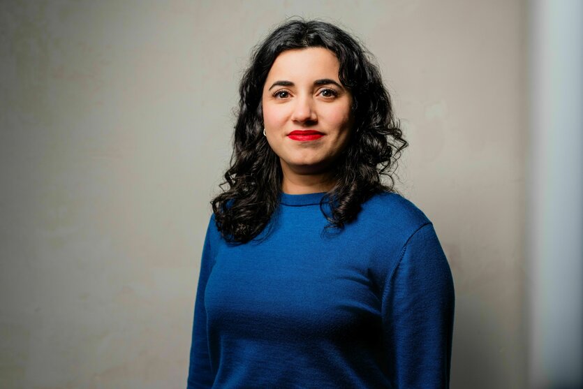 Misbah Khan steht in einem blauen Pullover vor einer grauen Wand