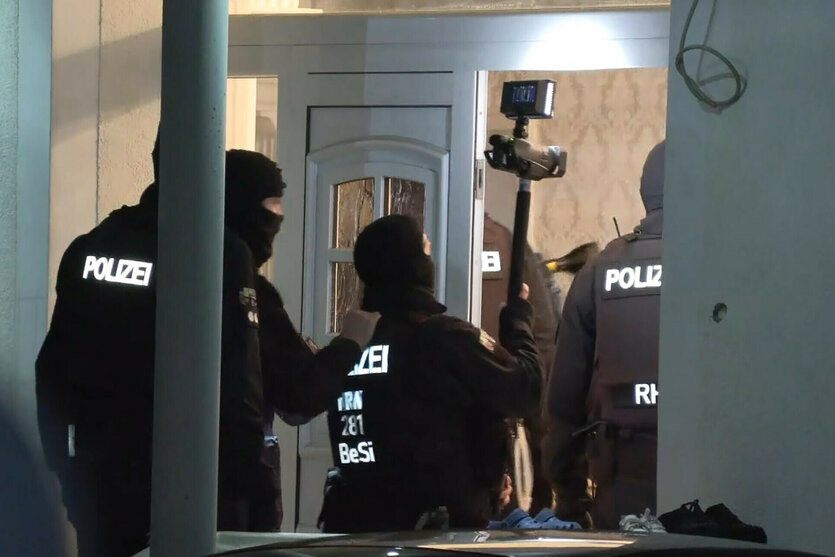Vermummte Polizisten betreten ein Haus