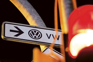 Vor einem Straßenschild mit der Aufschrift VW und einem Pfeil steht eine rote Ampel