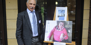 Ein Mann steht neben einem Foto, das sich auf einer Staffelei befindet. Es zeigt seine Tochter.