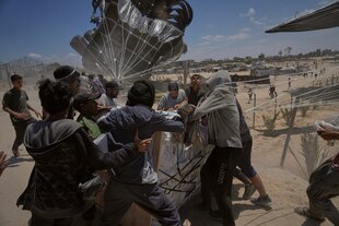 Humanitäre Güter mit noch geöffneten Fallschirmen. Männer greifen sich Pakete.