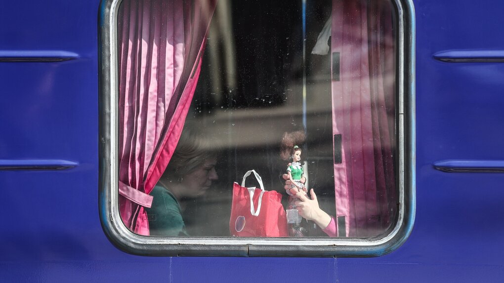 Durch ein Fenster eines ZUges sieht man die Hand eines Kindes, das eine Puppe hält