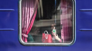 Durch ein Fenster eines ZUges sieht man die Hand eines Kindes, das eine Puppe hält