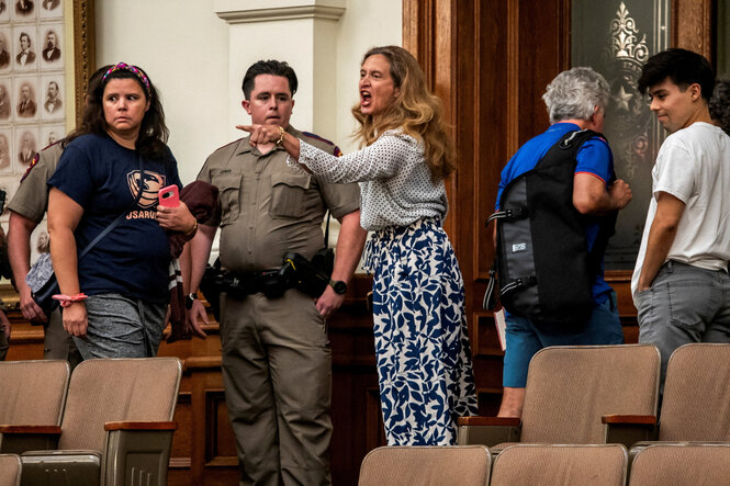 Auf den Zuschauerrängen des Parlaments von Texas ruft eine Frau wütend und mit den Finger zeigend Worte in Richtung Rednerpult. Neben ihr steht ein Sicherheitsbeamte und eine weitere Demonstrantin