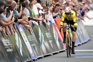 Ein Radfahrer fährt ins Ziel ein, am Rand Fans