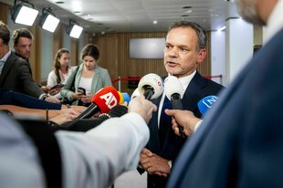 Caspar Veldkamp, anzugtragend, steht in einem Flur und spricht in ein Mikrofon, das jemand ihm hinhält
