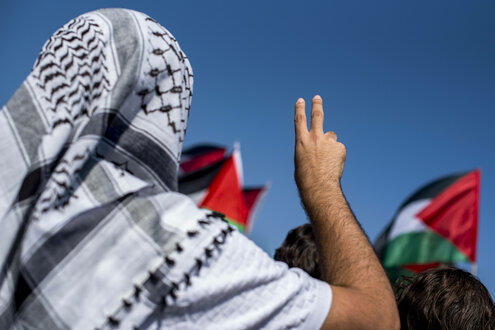 Mann mit Kufiya zeigt das Peace Zeichen mit den Fingern