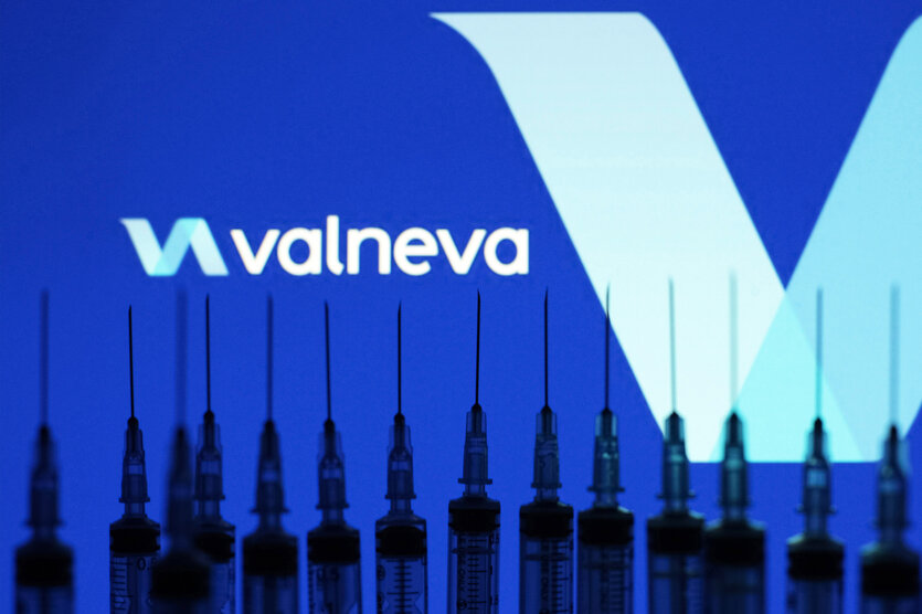 Das Firmenlogo von Valneva vor blauem Hintergrund, davor sind Spritzen in einer Reihe zu sehen