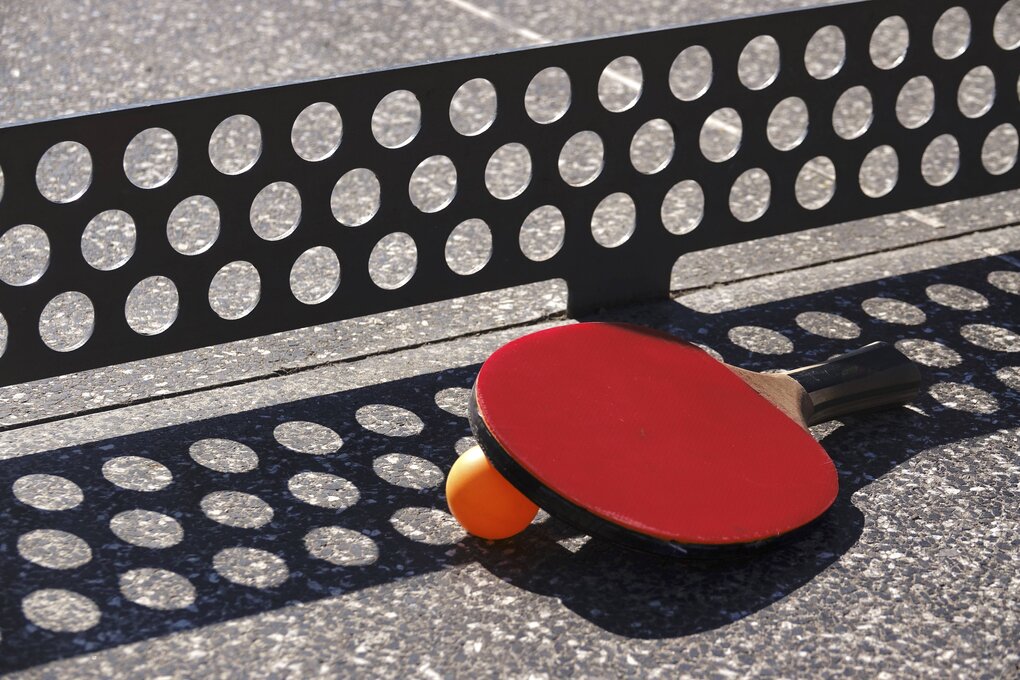 Ein Schläger und ein Ball liegen auf einer Steinplatte vor einem Gitter als Netz