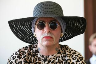 Person mit Bart, Lippenstift, Sonnenbrille und Hut