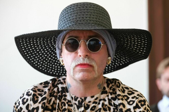Person mit Bart, Lippenstift, Sonnenbrille und Hut