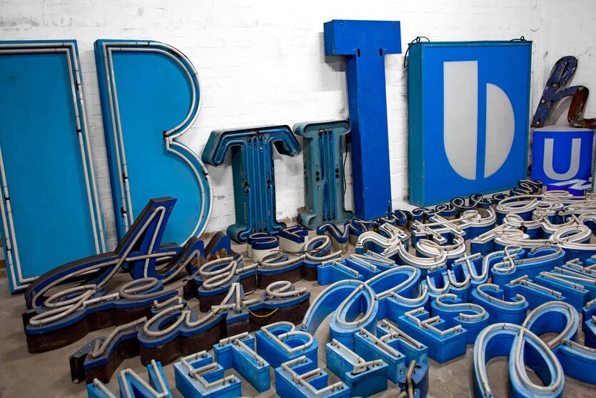 Ein I, ein B, ein T - unterschiedliche Buchstaben in Blau lehnen an der Wand und liegen auf dem Boden