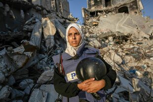 Porträt einer Journalistin aus Gaza, sie trägt ein Kopftuch und hält einen Helm im Arm