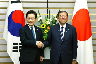Der japanische Ministerpräsident und der südkoreanische Präsident schütteln sich für die Kameras die Hände. Sie stehen vor ihren jeweiligen Landesflaggen