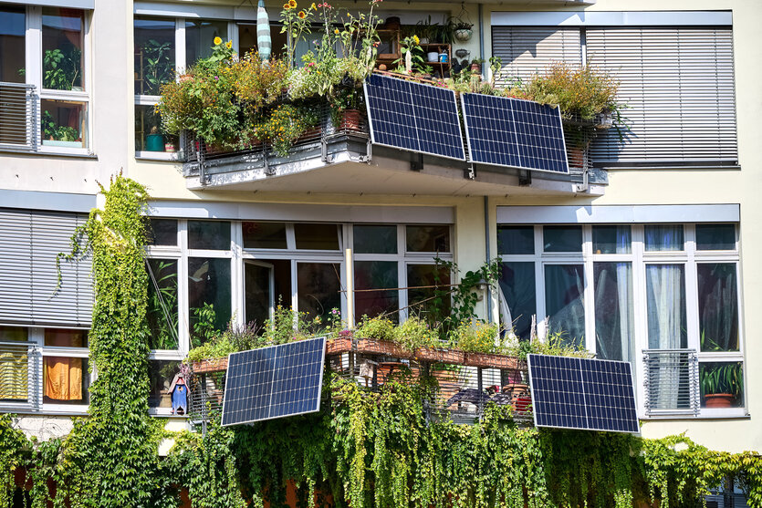 Ein begrüntes Haus mit Balkonen, an denen Photovoltaikanlagen befestigt sind