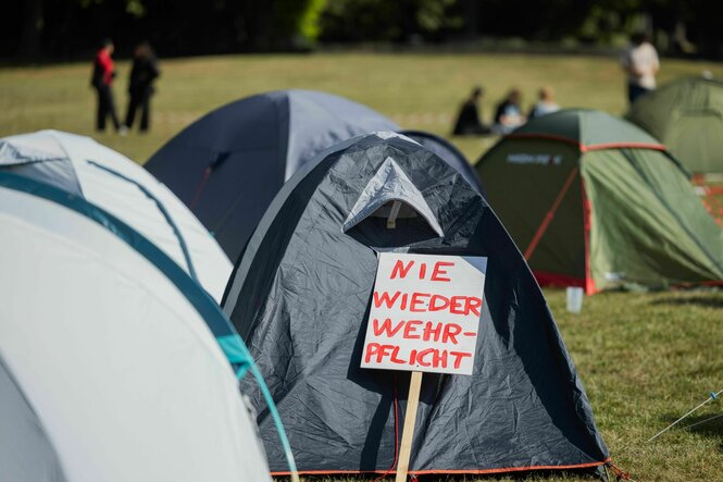 Kleine Zelte stehen auf einer Wiese, an einem hängt ein kleines Schild: Nie wieder Wehrpflicht