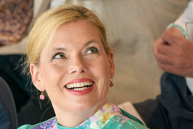Das Bild zeigt Julia Klöckner mit blonden Haaren, die zu einem Knoten zurückgebunden sind. Sie trägt Ohrringe und ein bunt gemustertes Oberteil in Pastellfarben, sie lächelt breit und schaut schräg nach oben.