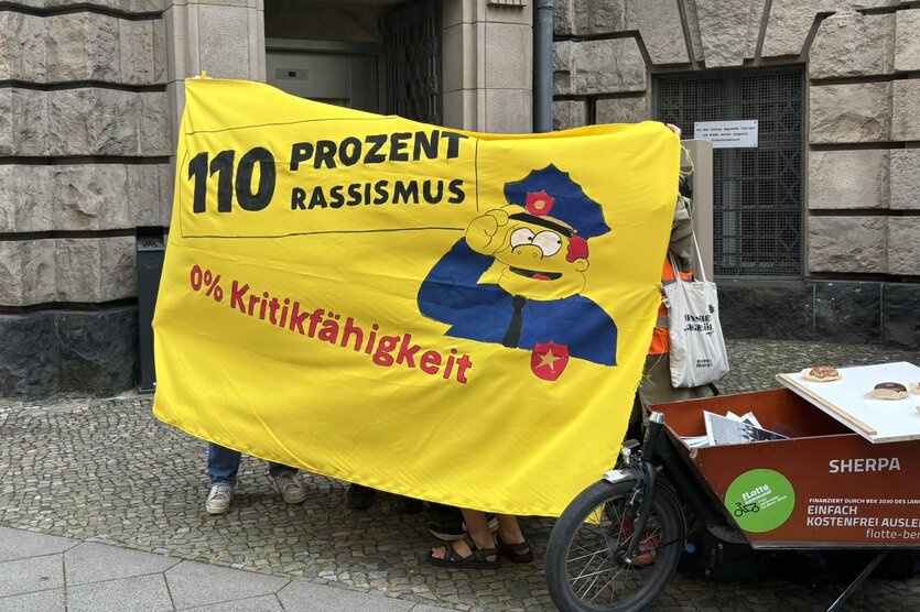 Ein Plakat vor einem Gerichtsgebäude: „110 Prozent Rassismus – 0% Kritikfähigkeit“, daneben ein Lastenfahrrad