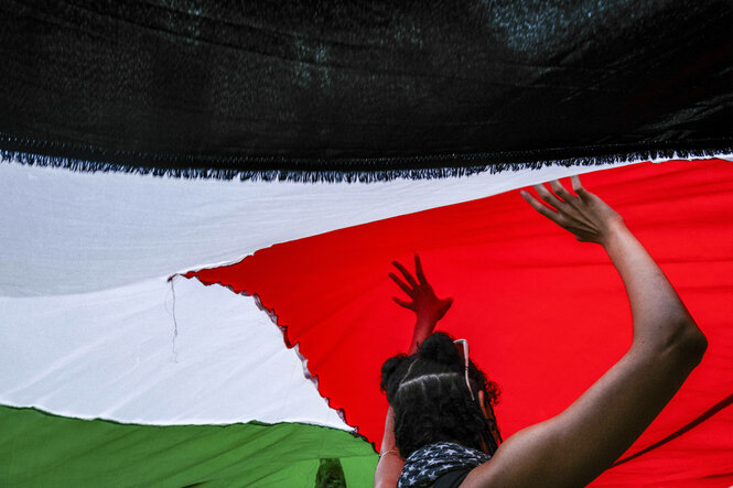 Pro-Palästina Demonstrierende halten eine riesige palästinensische Flagge hoch, wir blicken von unten nach oben, die Flagge füllt das Bild und eine Person hält sie von unten