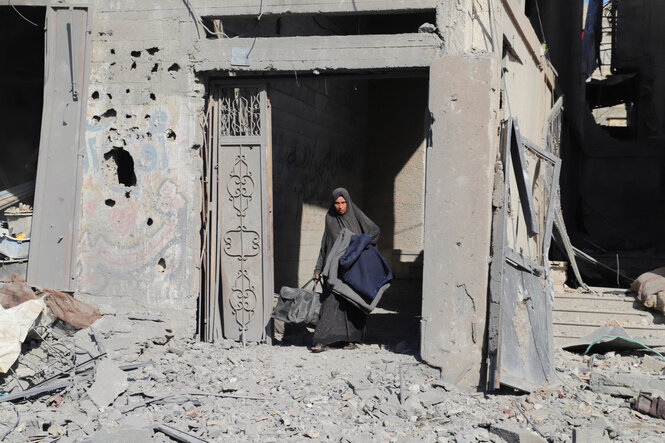 Eine Frau tritt aus einer Hausruine, sie hat einen Koffer in der Hand