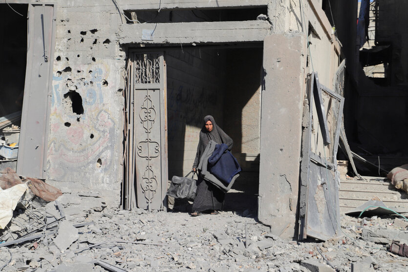 Eine Frau tritt aus einer Hausruine, sie hat einen Koffer in der Hand